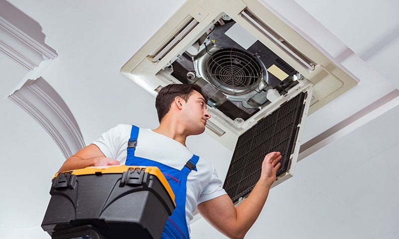 Technician holds tool box while inspecting a ceiling cassette AC unit