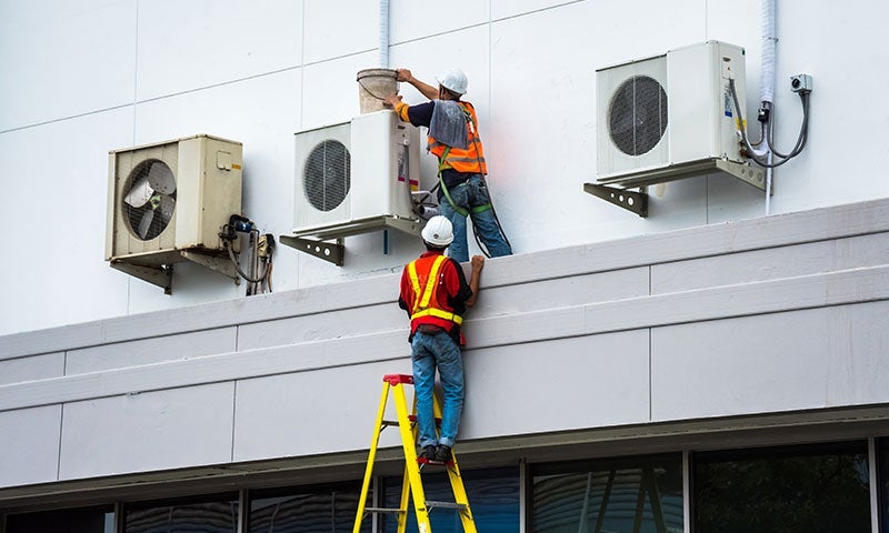 HVAC technicians climb ladder to service three commercial AC units