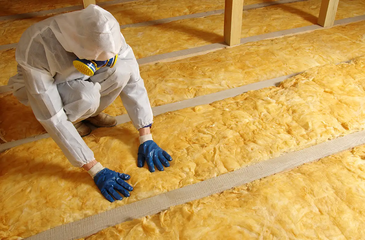 A person in a protective suit and respirator installing attic insulation