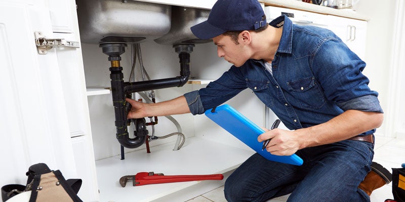 Plumber inspecting and documenting the plumbing connections under a kitchen sink