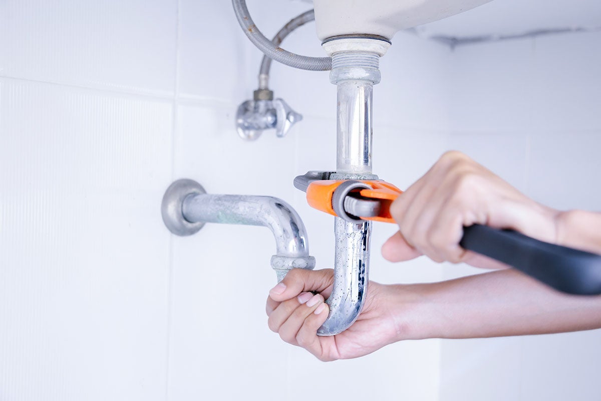 Person using an adjustable wrench to tighten or loosen a chrome metal sink drain pipe (P-trap)