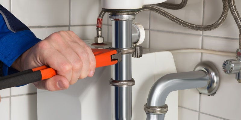 Plumber using a wrench to tighten or loosen a chrome sink drain pipe