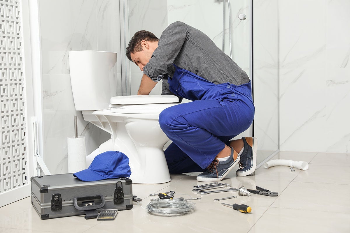 Plumber repairing a toilet in a modern bathroom with tools on the floor
