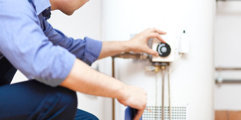 Person adjusting the temperature dial or thermostat on a white water heater or boiler